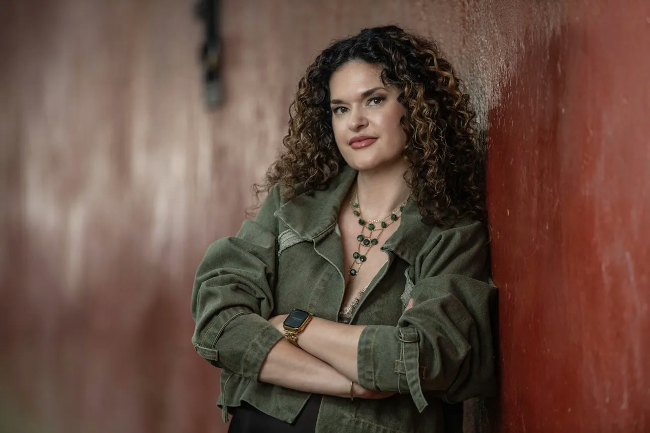 Dr. Brighten with arms crossed, leaning against a red clay wall in an olive jacket