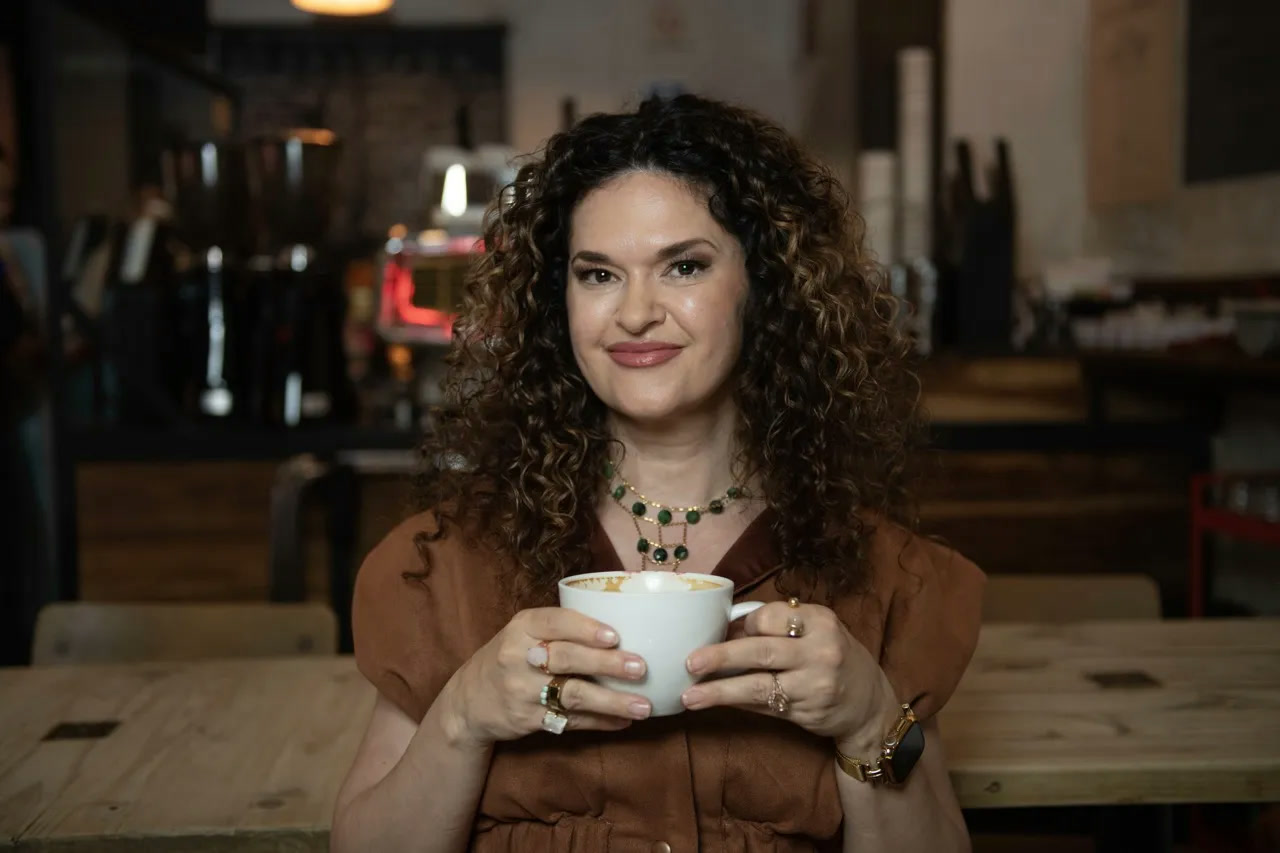 Dr. Brighten smiling over a cup of coffee at a café table, wearing a rust-colored dress